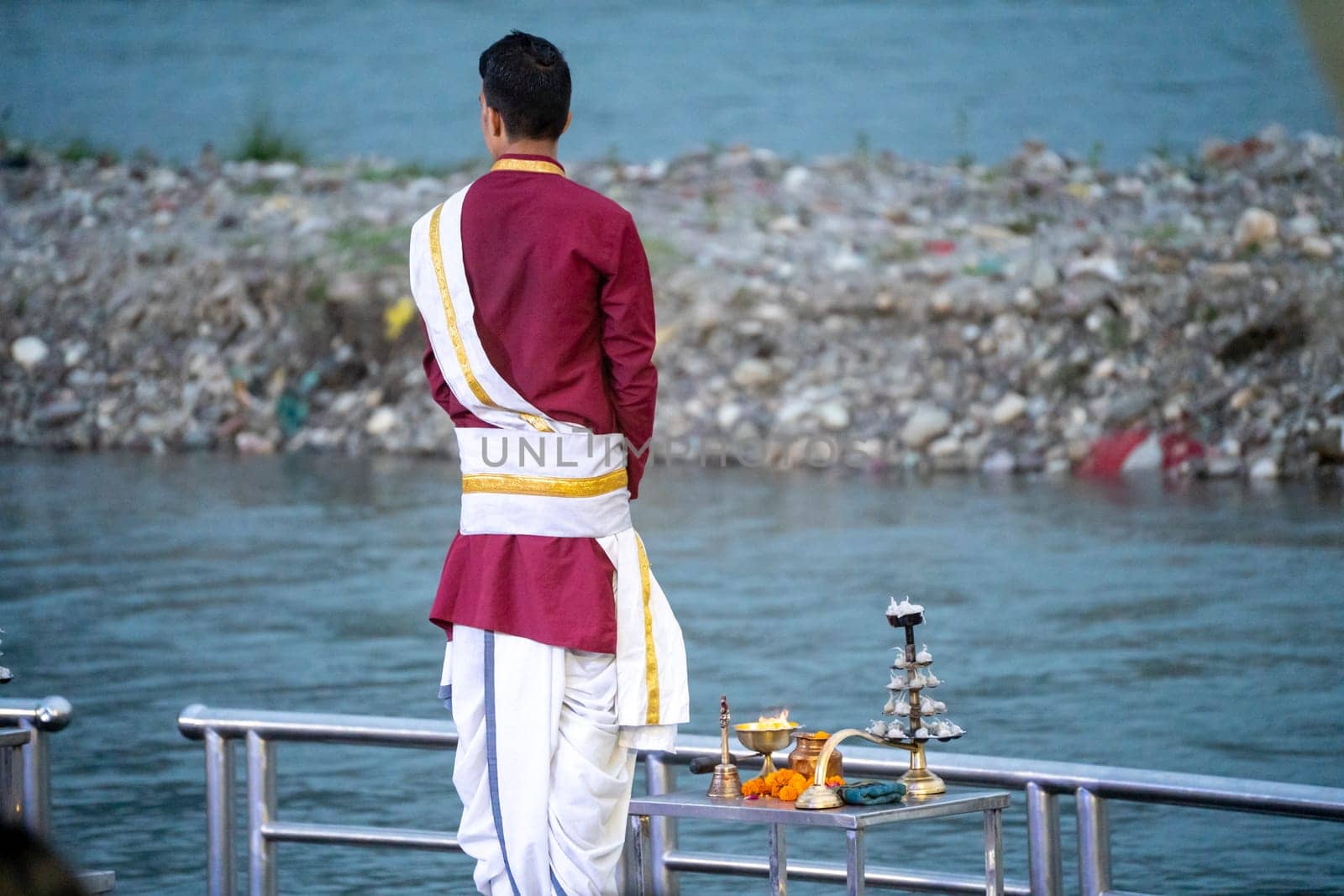 Priest in red and white chanting hymns to the holy river ganga with a lit oil diya lamp giving off smoke as part of the evening aarti prayer performance at triveni ghat