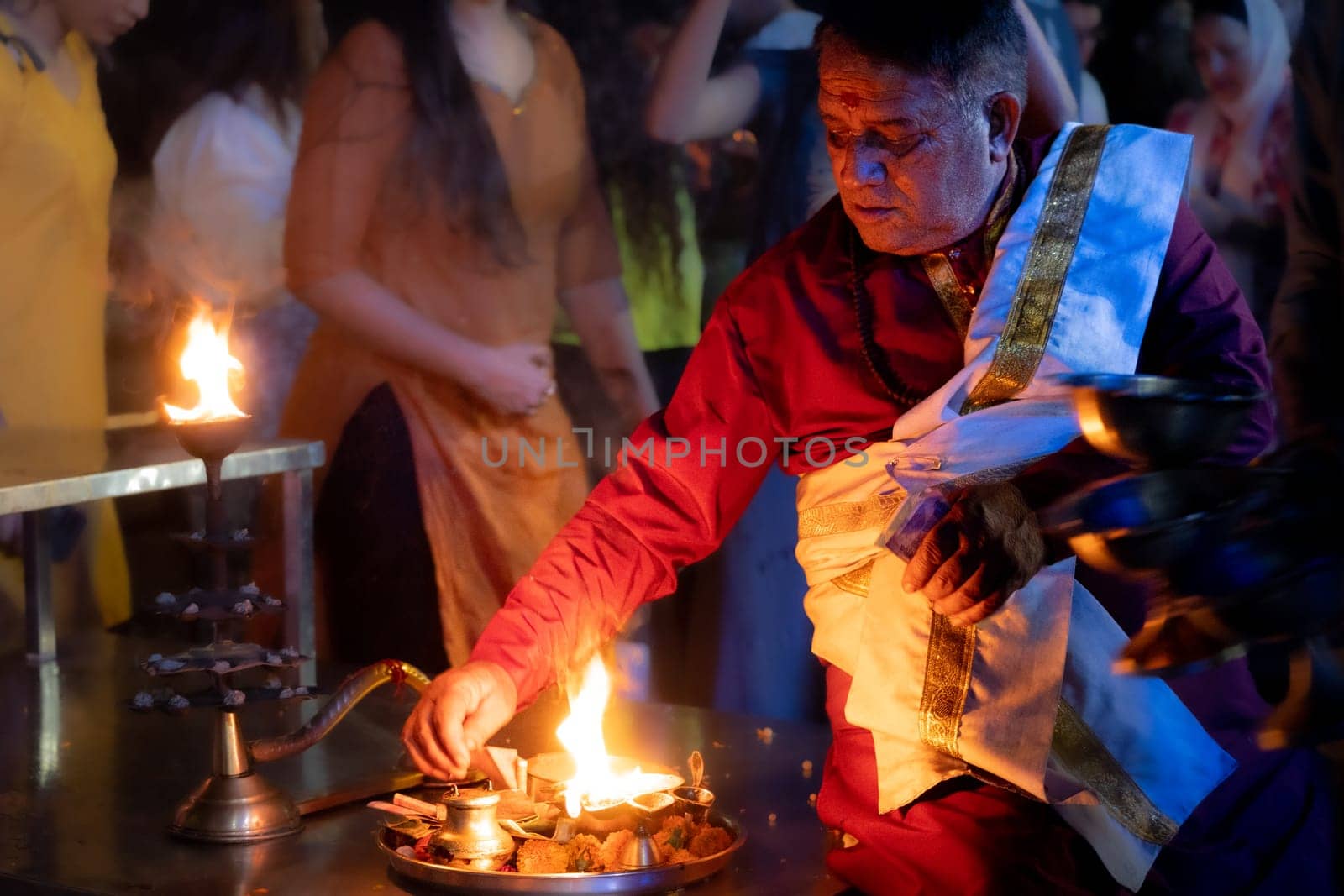 Rishikesh, India - 29th Apr'23: hindu priest sitting on the bank of ganga river lit from one side by the fire from an oil lamp a key component in Hinduism religion in India