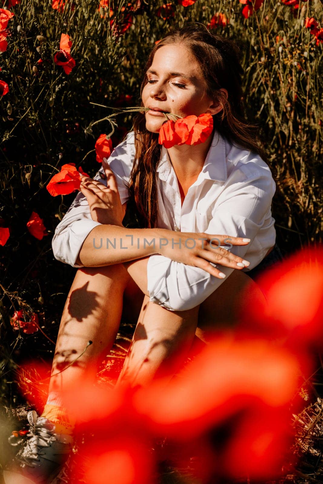 Woman poppies field. Happy woman is resting in the rays of the sun sitting in the poppy field