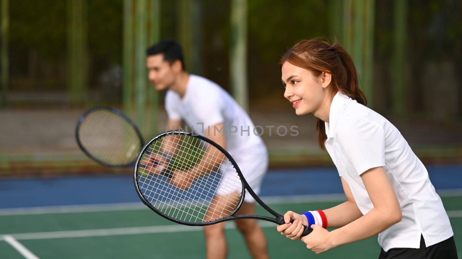Two tennis players crouching in ready position and holding racket while waiting for serving ball during a competitive match.