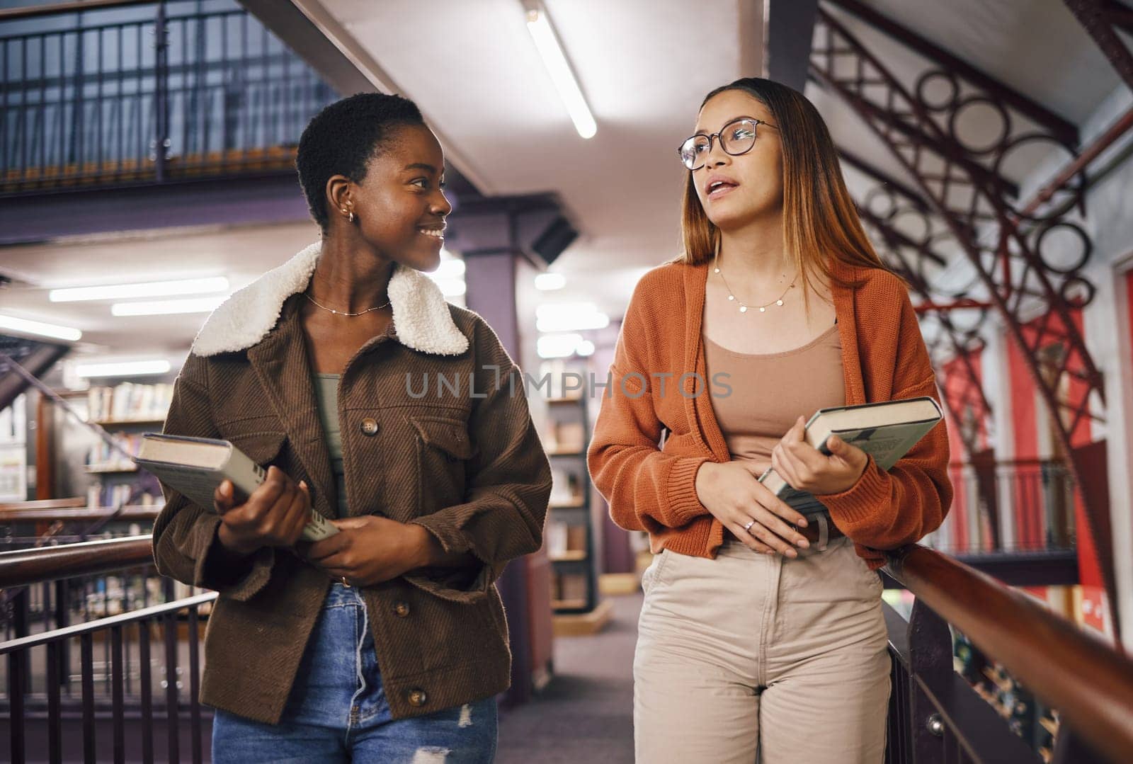 College students, library books and women talking about education and learning together at university. Friends having conversation about knowledge, studying and research on scholarship while walking by YuriArcurs