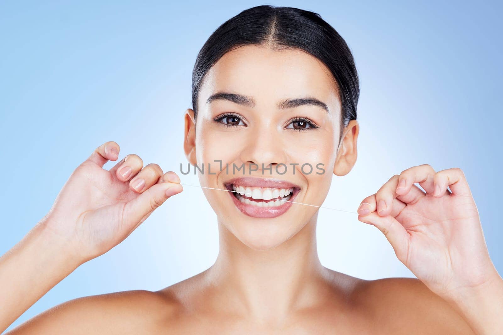 Face, flossing teeth and hygiene with woman, dental and beauty with grooming and mouth care on blue background. Hands, string and healthy gums with fresh breath, health and skin glow in portrait.