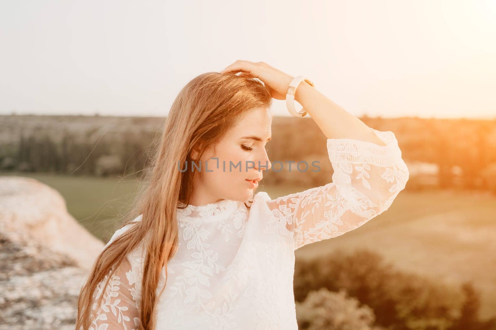 Romantic beautiful bride in white dress posing with sea and mountains in background. Stylish bride standing back on beautiful landscape of sea and mountains on sunset