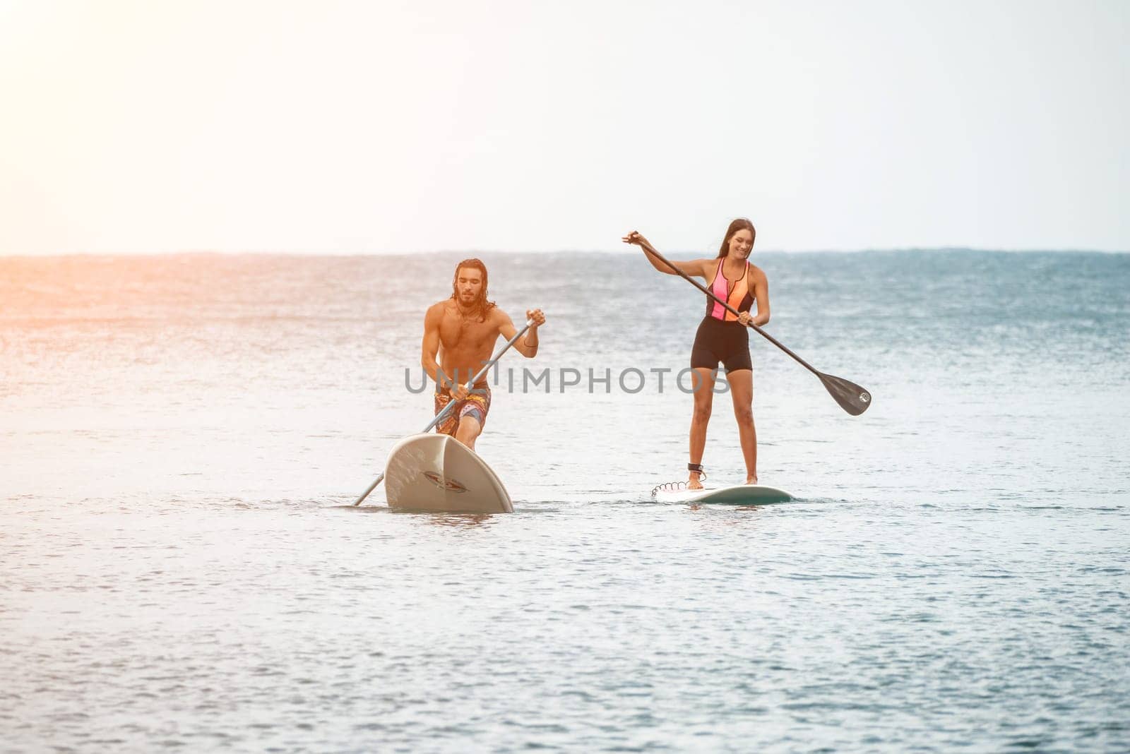 Sea woman and man on sup. Silhouette of happy young woman and man, surfing on SUP board, confident paddling through water surface. Idyllic sunset. Active lifestyle at sea or river