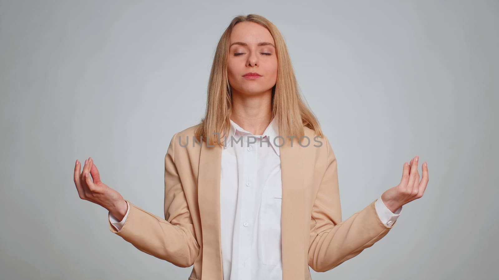Keep calm down, relax, inner balance. Business woman breathes deeply with mudra gesture, eyes closed, meditating with concentrated thoughts, peaceful mind. Female girl in suit on gray background