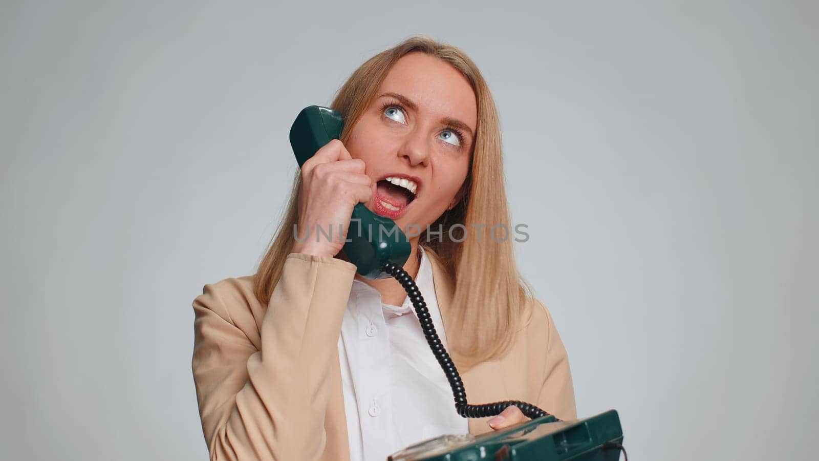 Portrait of young businesswoman talking on wired vintage telephone of 80s, fooling, making silly faces, joke, prank. Crazy female girl in formal suit. Pretty woman isolated on gray studio background