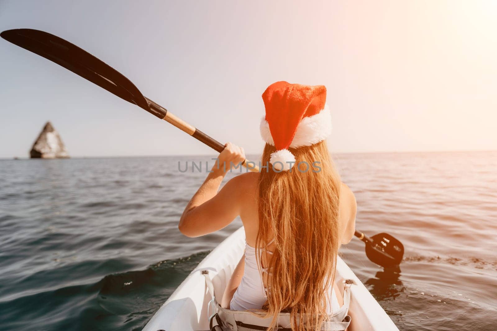 Woman in kayak back view. Happy young woman with long hair floating in transparent kayak on the crystal clear sea. Summer holiday vacation and cheerful female people relaxing having fun on the boat