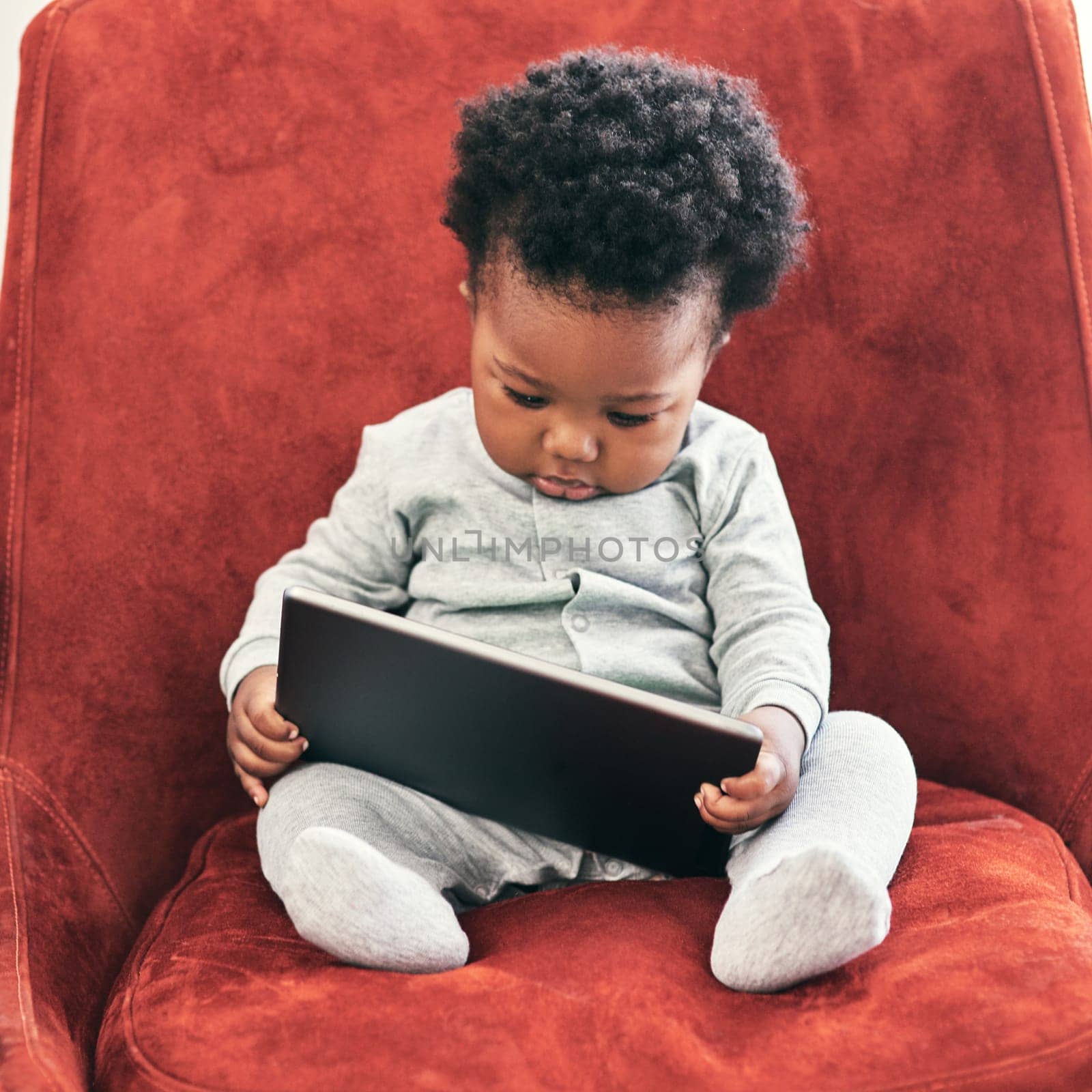 I need to check my emails.... Shot of a little baby boy sitting in a chair holding a digital tablet. by YuriArcurs