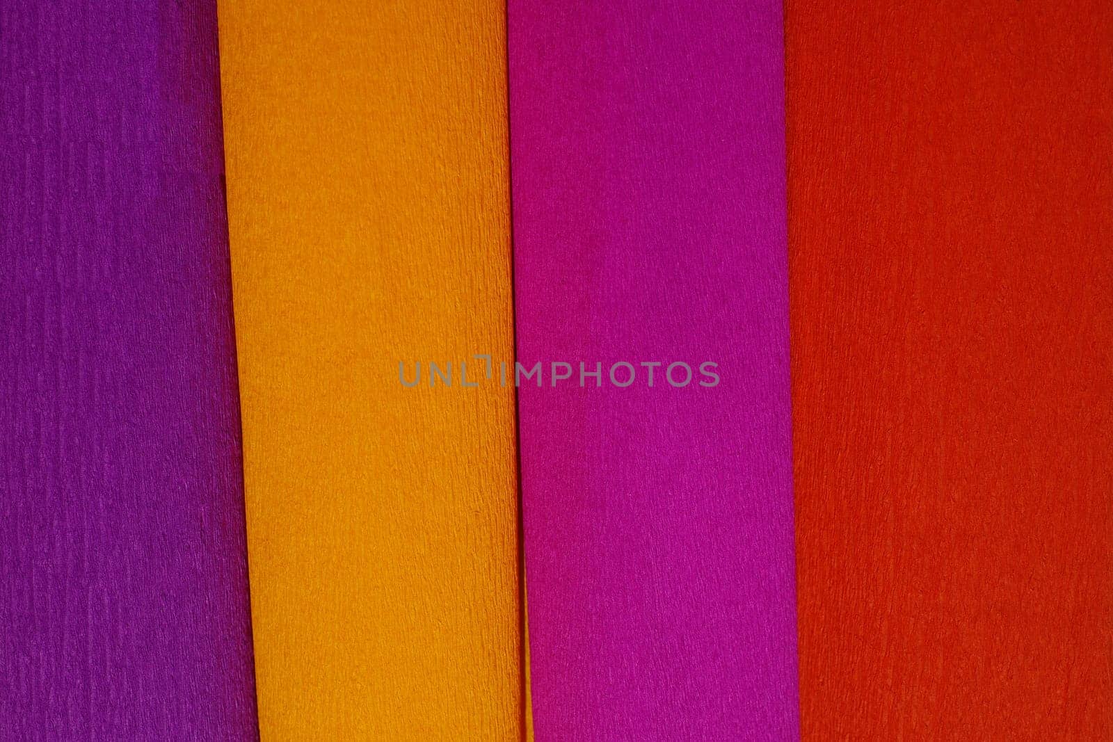 Rolls of crepe paper lying next to each other in the colors purple, red, orange, lilac