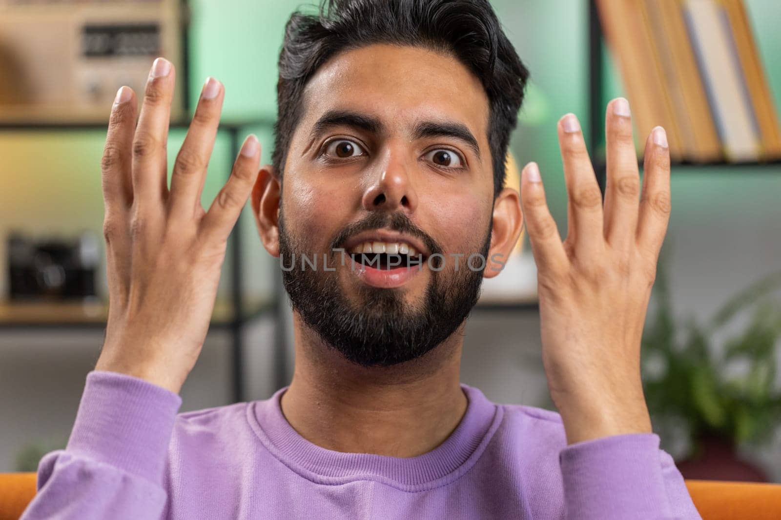 Oh my God, Wow. Young indian man surprised looking at camera with big eyes, shocked by sudden victory, good win news, celebrating. Portrait of excited amazed hindu guy at home apartment room on sofa
