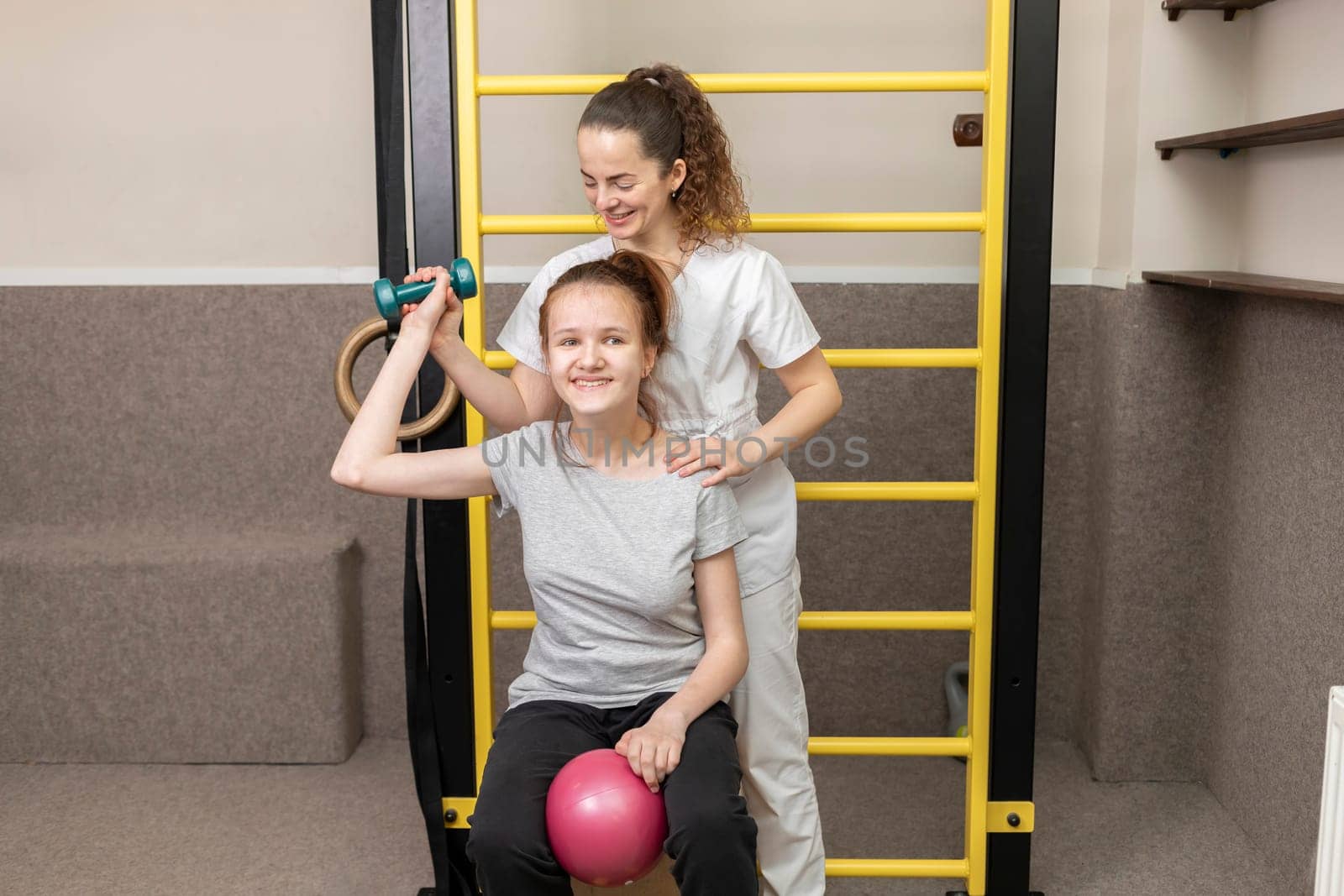 Physician Helps Happy Disabled Child Raise Dumbbell, Do Physical Exercises In Rehabilitation Room. Kid With Special Needs In Gym. Rehabilitation. Horizontal plane. by netatsi