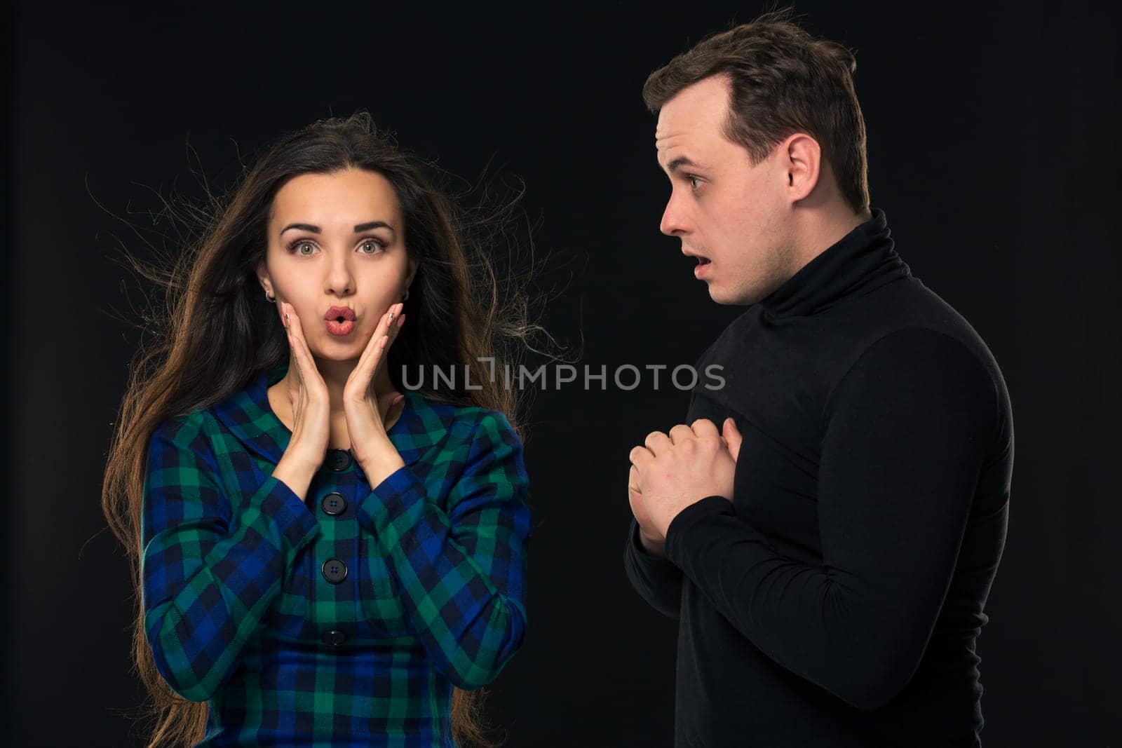 Excited scared nervous woman look into camera, man stand by side, have eyes full in disbelief. On black background by nazarovsergey