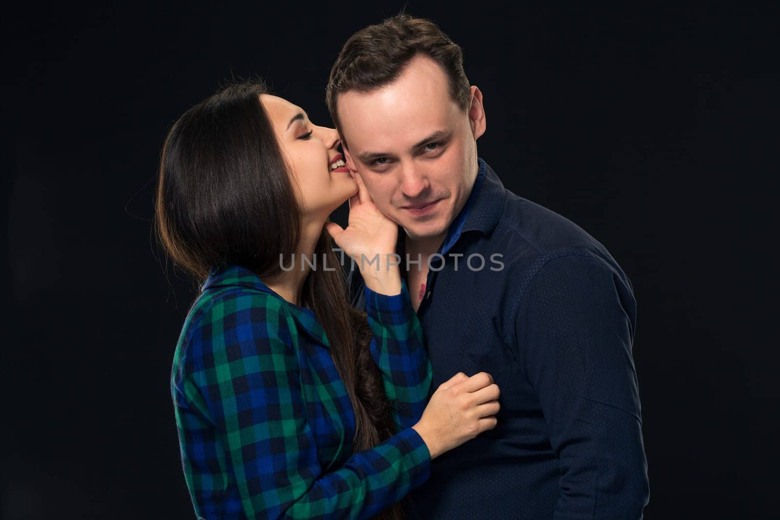 Woman whispering into a man's ear on black background