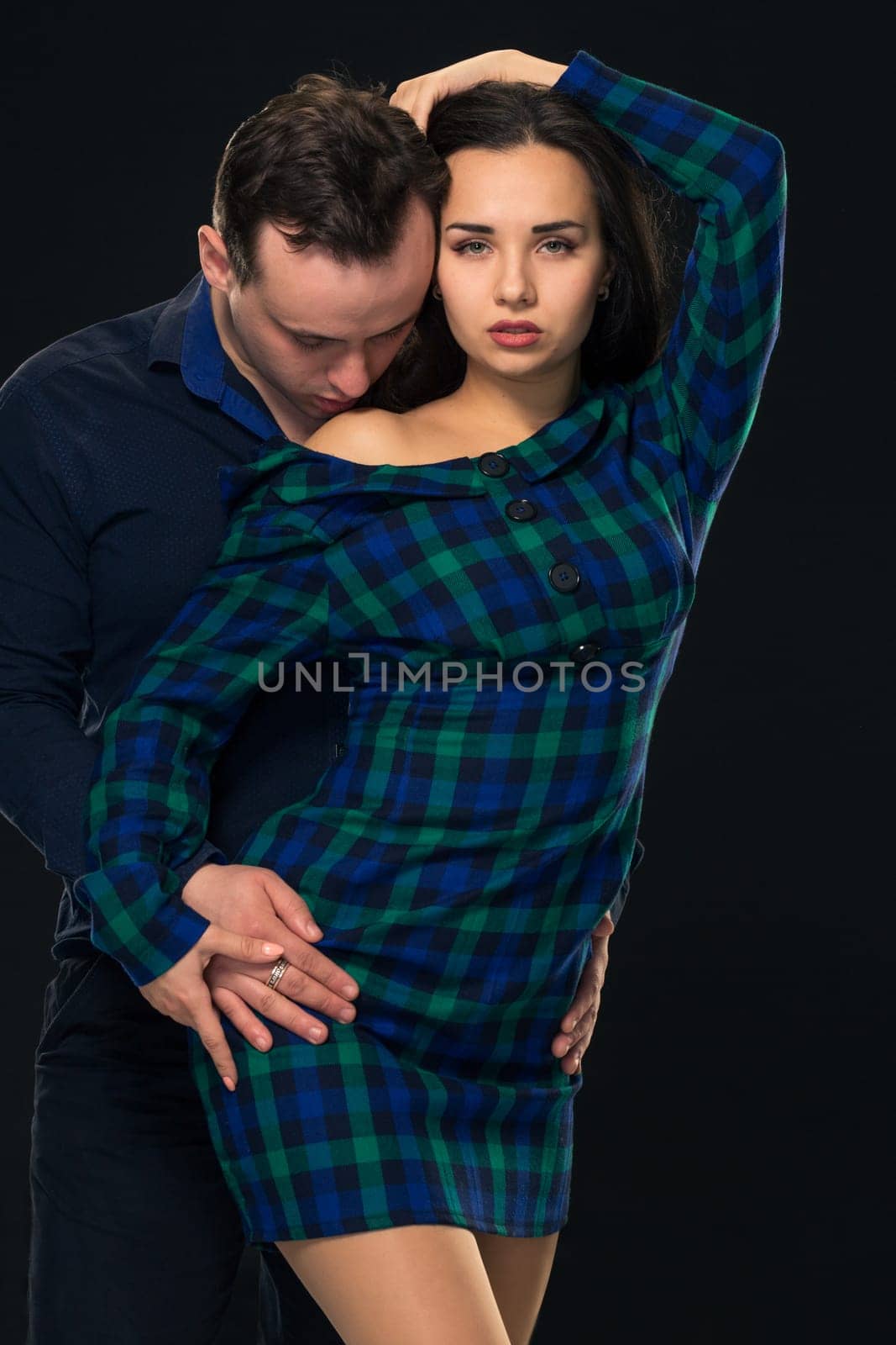 Couple posing in studio. On black background. Young woman in blue checkered dress