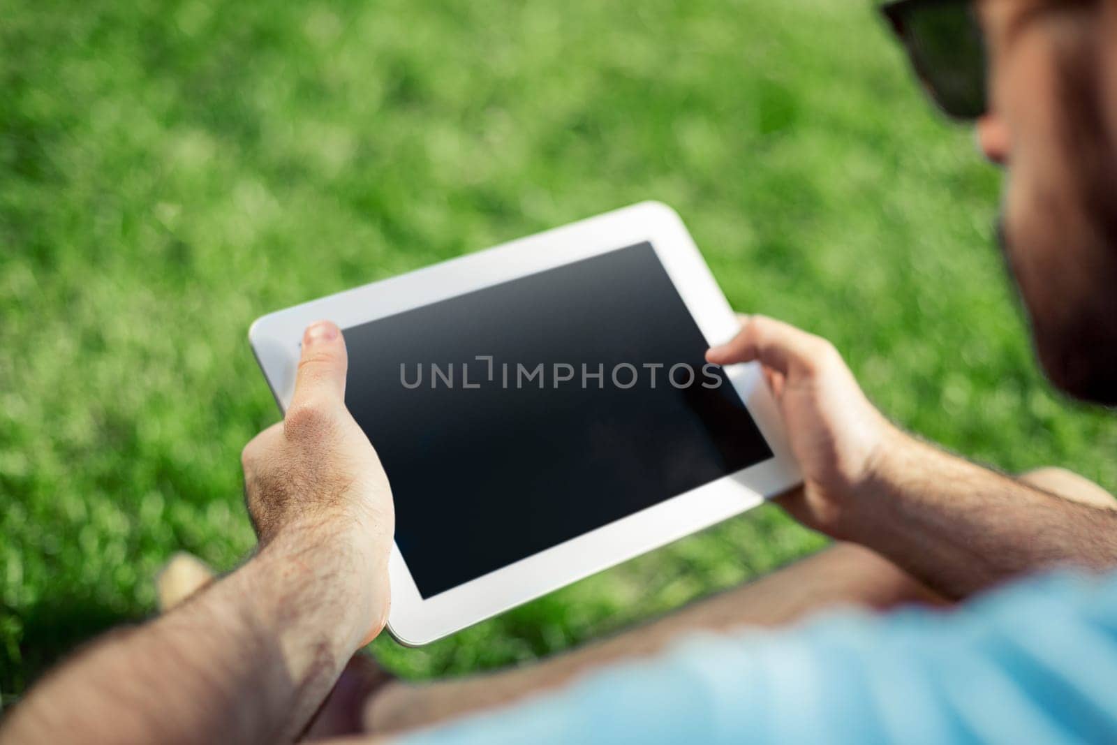 Young man using and typing tablet computer in summer grass. by nazarovsergey