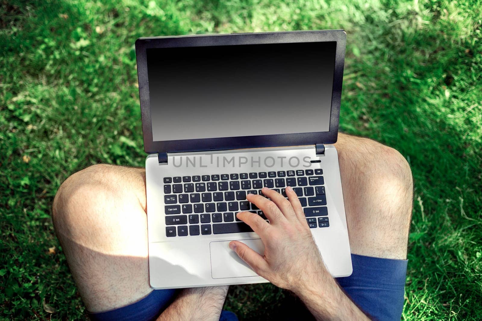 Young blogger sitting on grass and working with laptop. Copy space