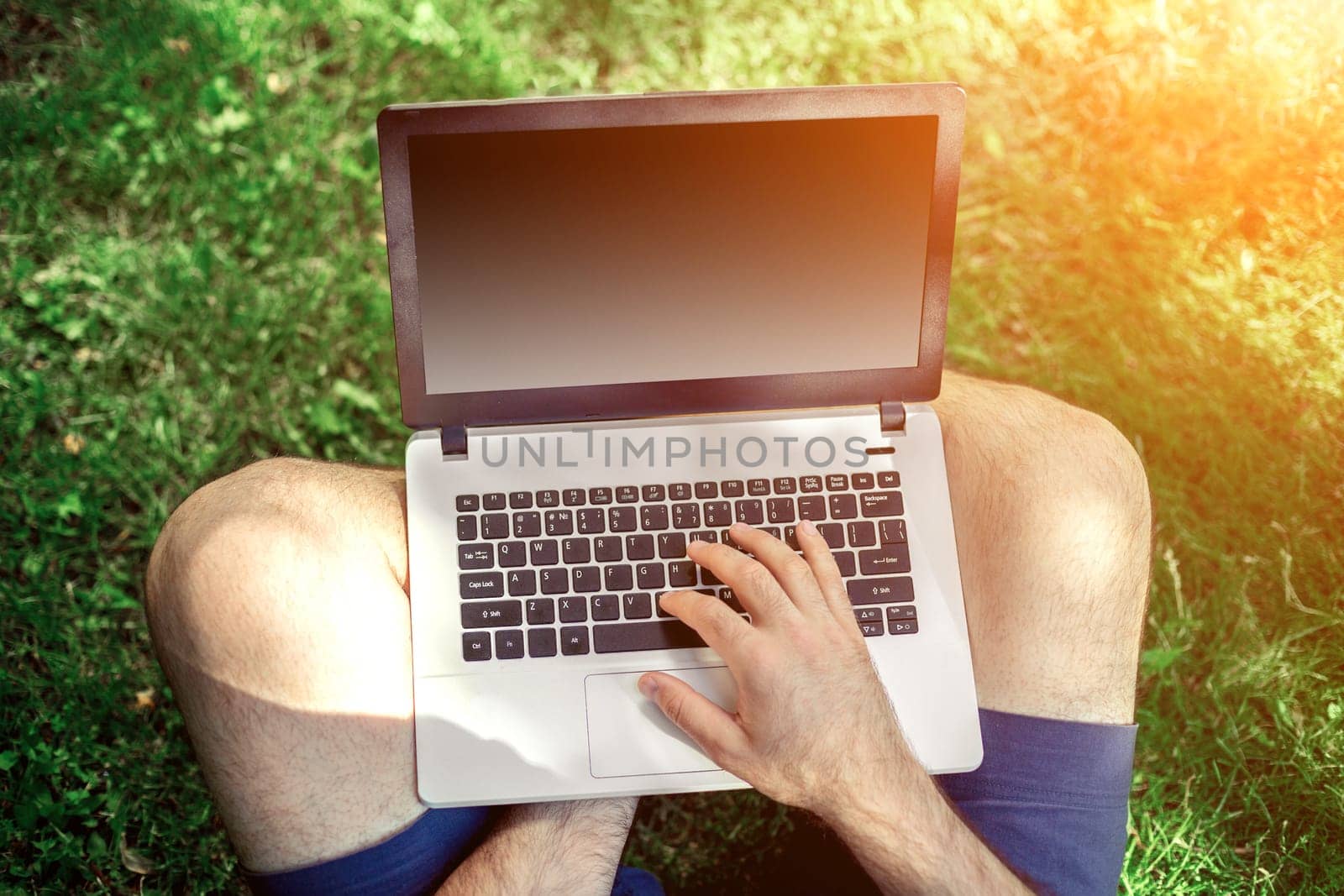 Young blogger sitting on grass and working with laptop. Copy space. Sun flare