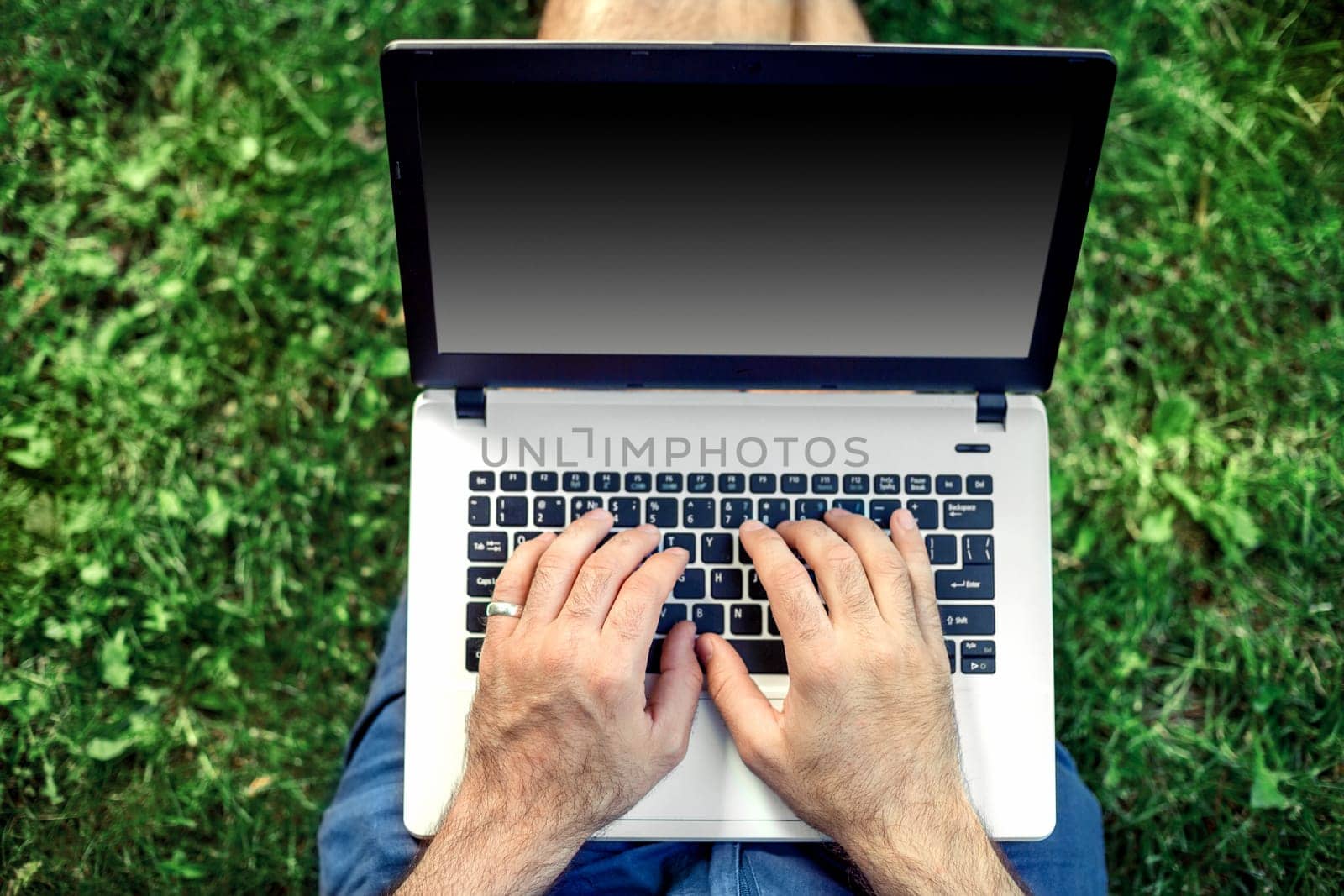 Young blogger sitting on grass and working with laptop. Copy space