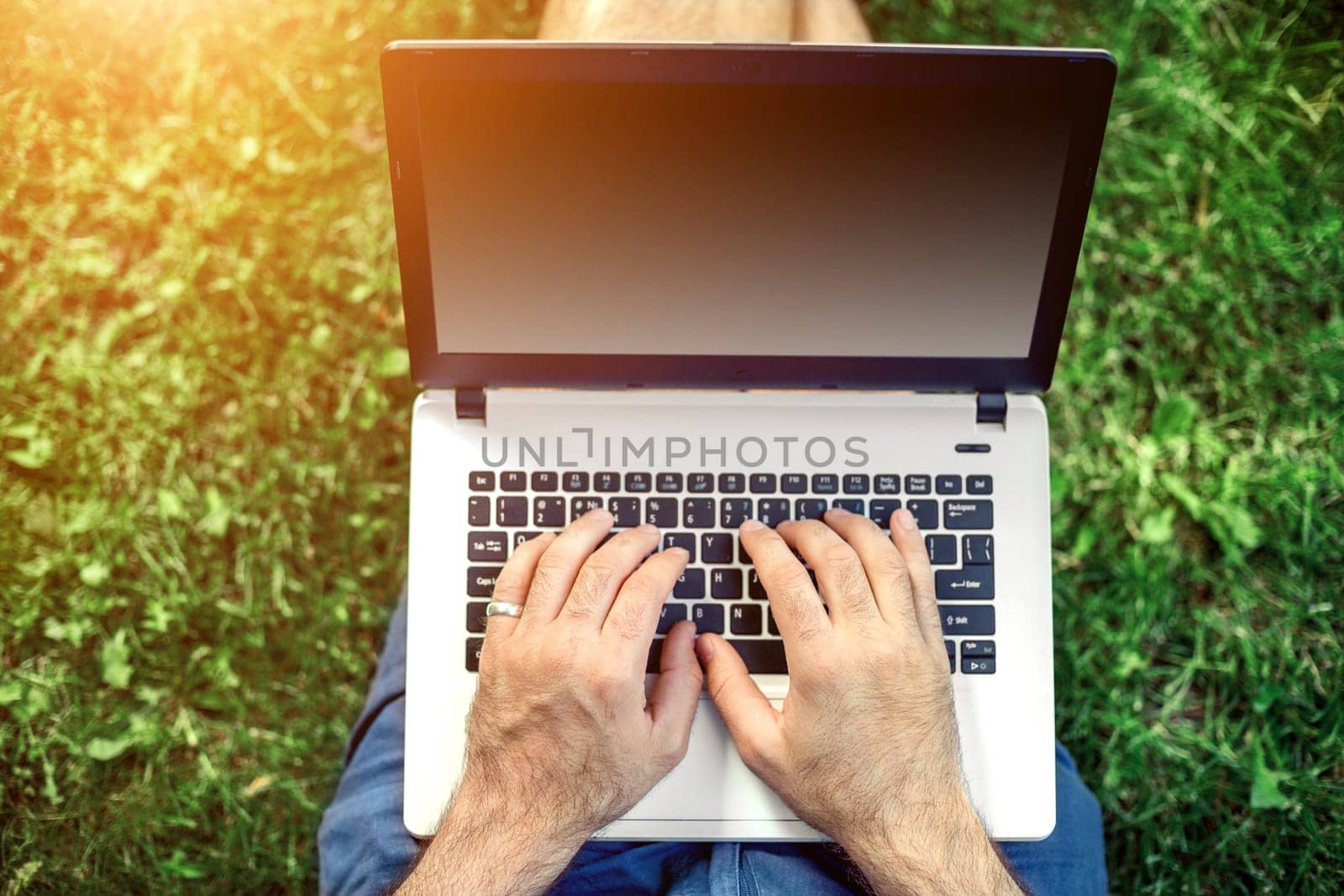 Young blogger sitting on grass and working with laptop. Copy space. Sun flare