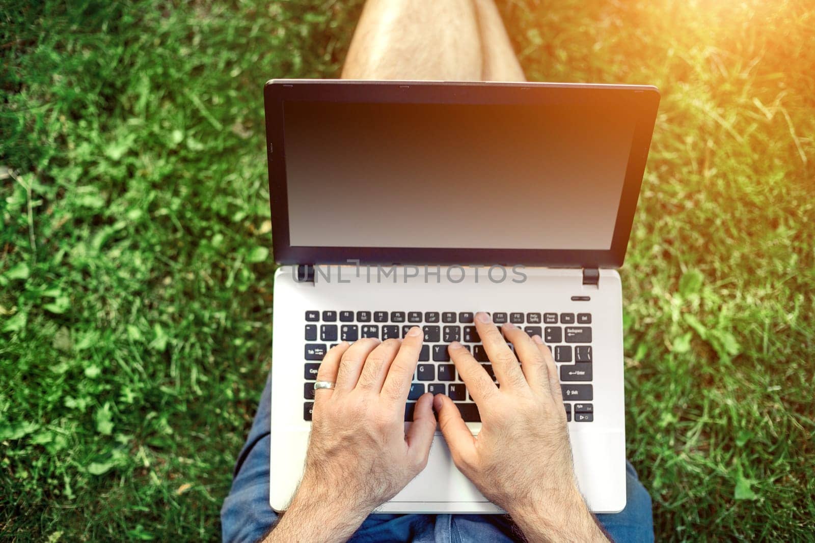 Young blogger sitting on grass and working with laptop. Copy space. Sun flare