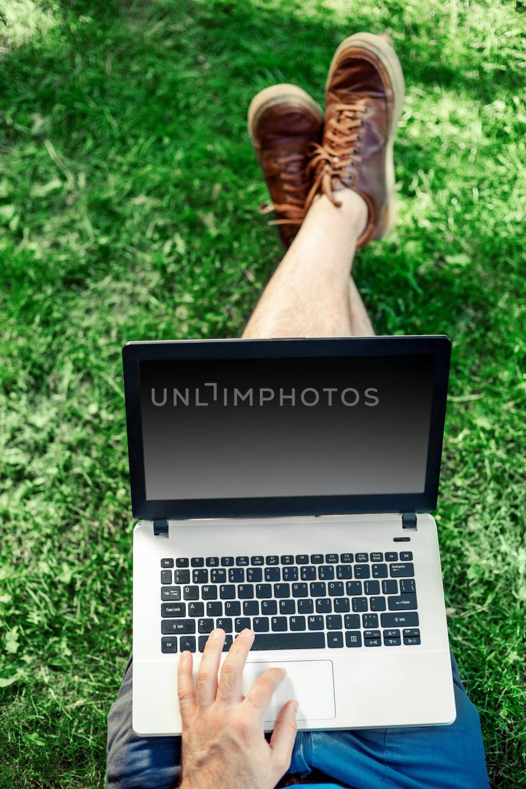 Young blogger sitting on grass and working with laptop. Copy space