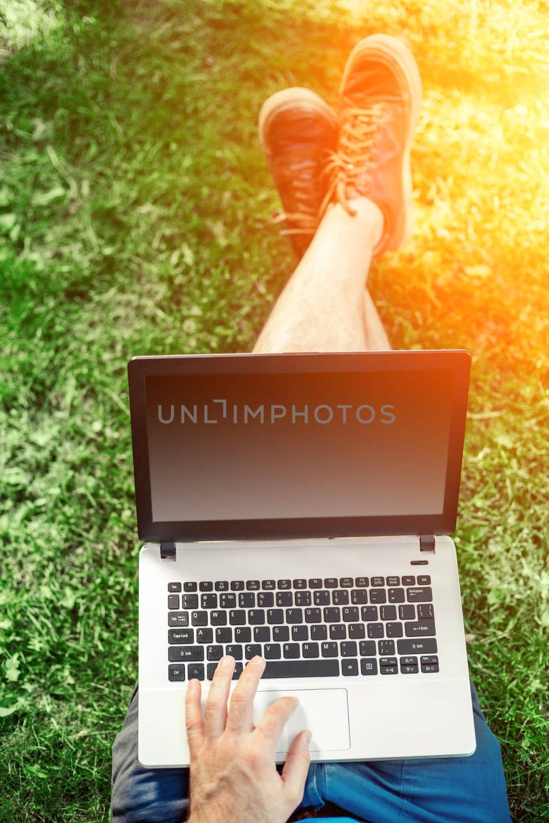 Young blogger sitting on grass and working with laptop by nazarovsergey