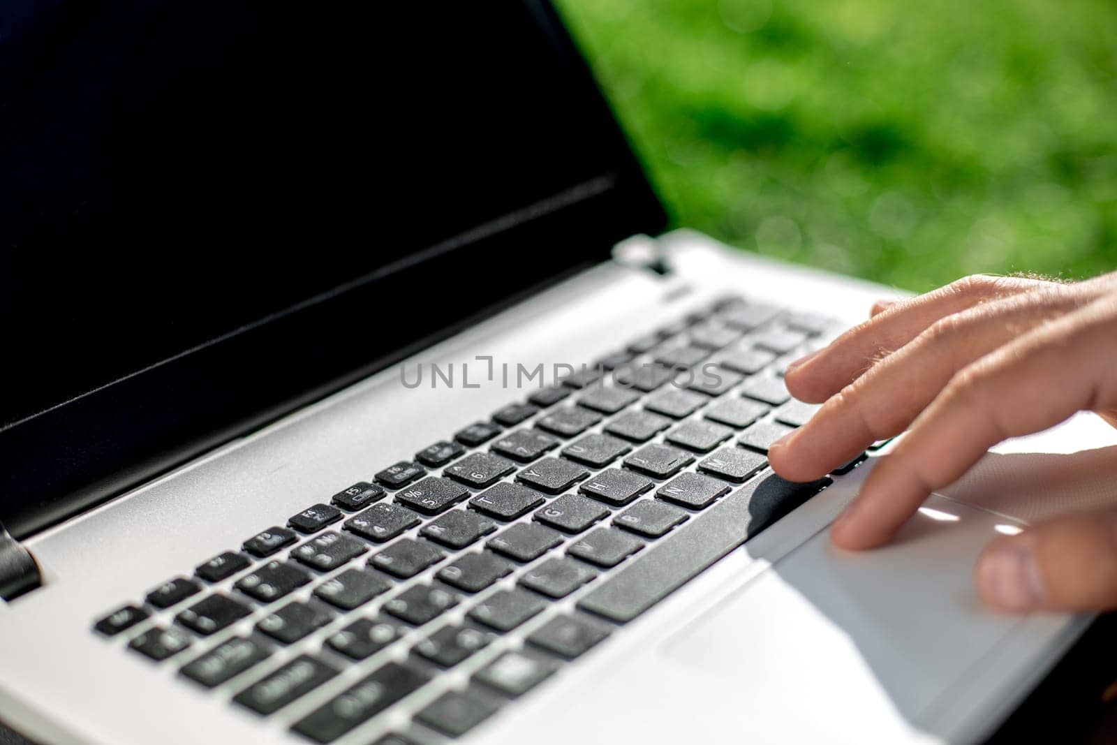 Close-up shot of handsome man's hands touching laptop computer's screen. Businessman using a laptop computer and sitting on the ground.