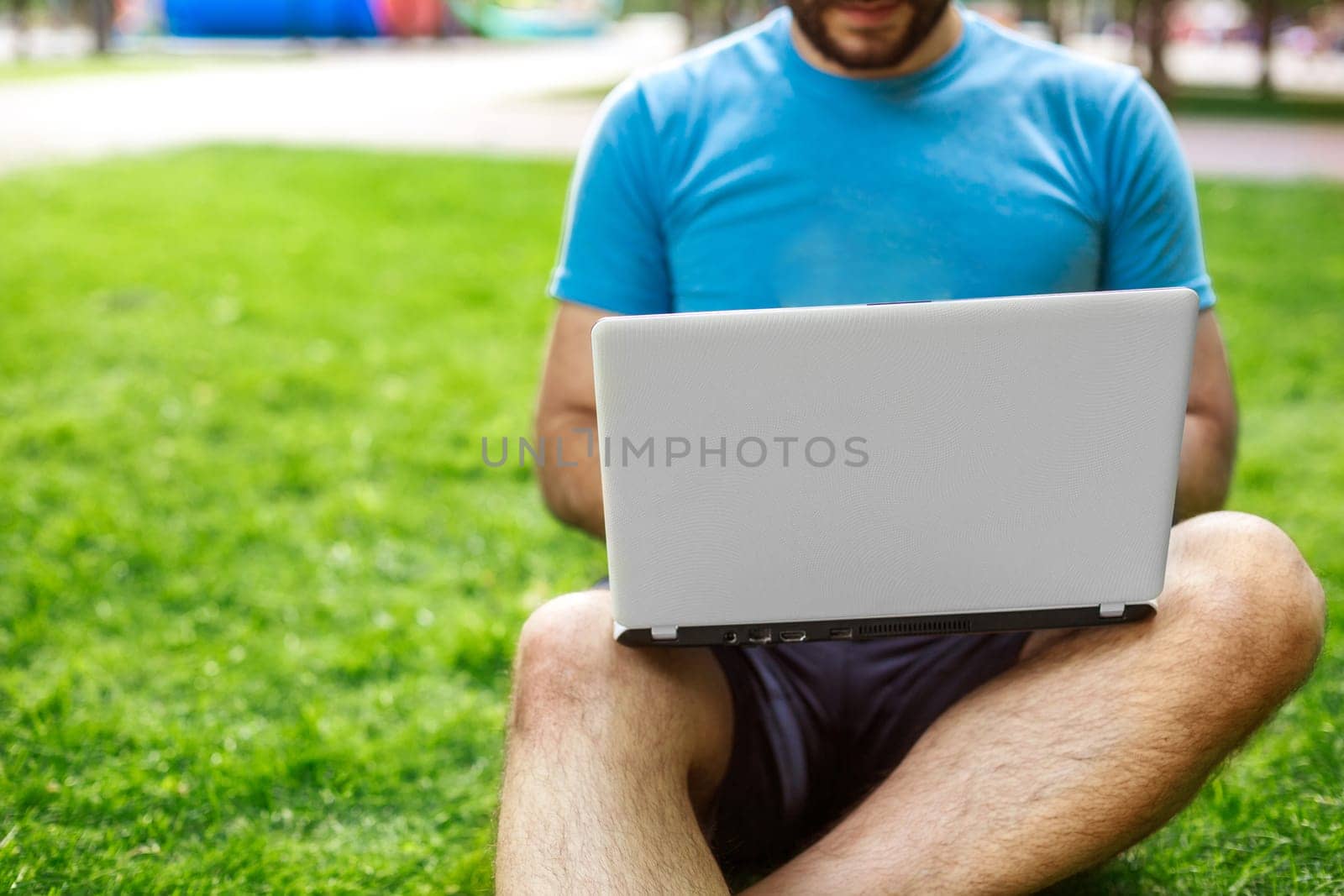 Young man using and typing laptop computer in summer grass. Freelancer working in outdoor park