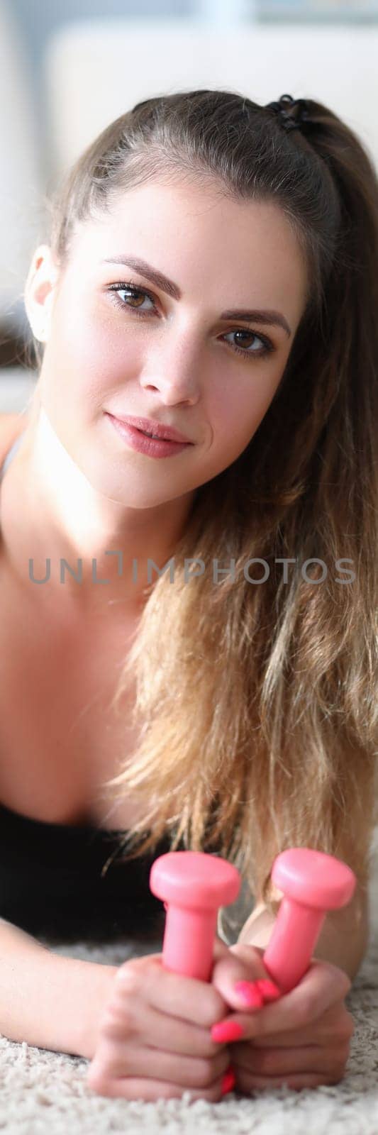 Portrait of beautiful young woman lies on floor with dumbbells. Home fitness and health concept