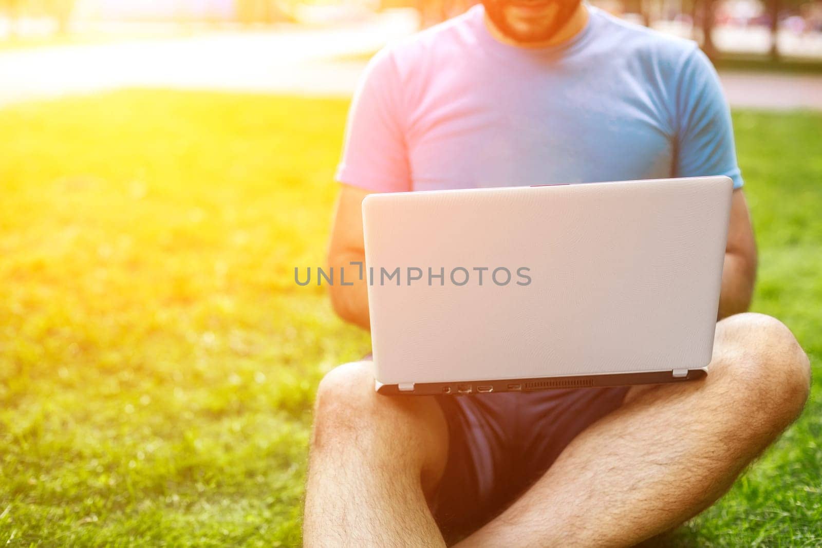 Young man using and typing laptop computer in summer grass. by nazarovsergey