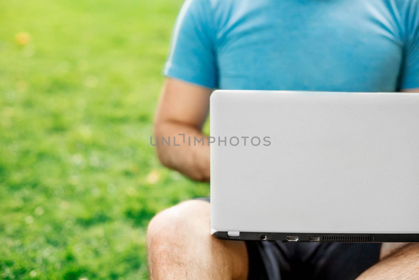 Young man using and typing laptop computer in summer grass. Freelancer working in outdoor park