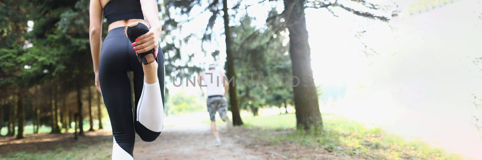 Rear view of a young fitness woman stretching leg outdoors in morning in park by kuprevich