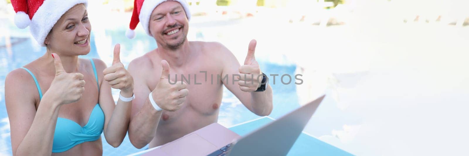 Family of bloggers in santa claus hats show thumbs up in laptop monitor standing in pool by kuprevich