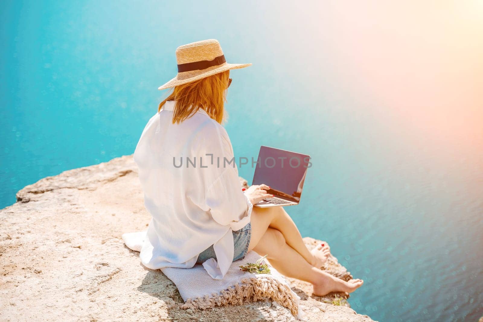 Freelance woman working on a laptop by the sea, typing away on the keyboard while enjoying the beautiful view, highlighting the idea of remote work. by Matiunina