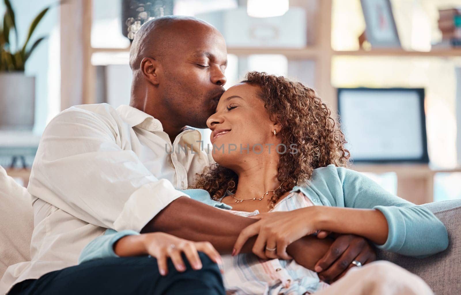 Love, kiss and couple relax on sofa for bonding, quality time and happiness together at home. Marriage, relationship and interracial man and woman on couch for calm, romance and embrace on weekend by YuriArcurs