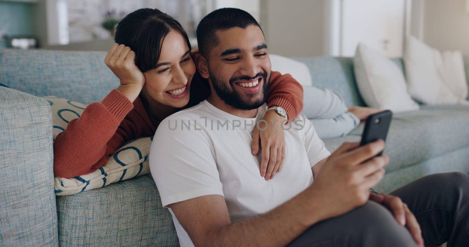 Couple, phone and laughing at meme on social media or internet joke and relax in a living room couch in a home. Sofa, cellphone and people streaming online comedy on a smartphone in a house together by YuriArcurs