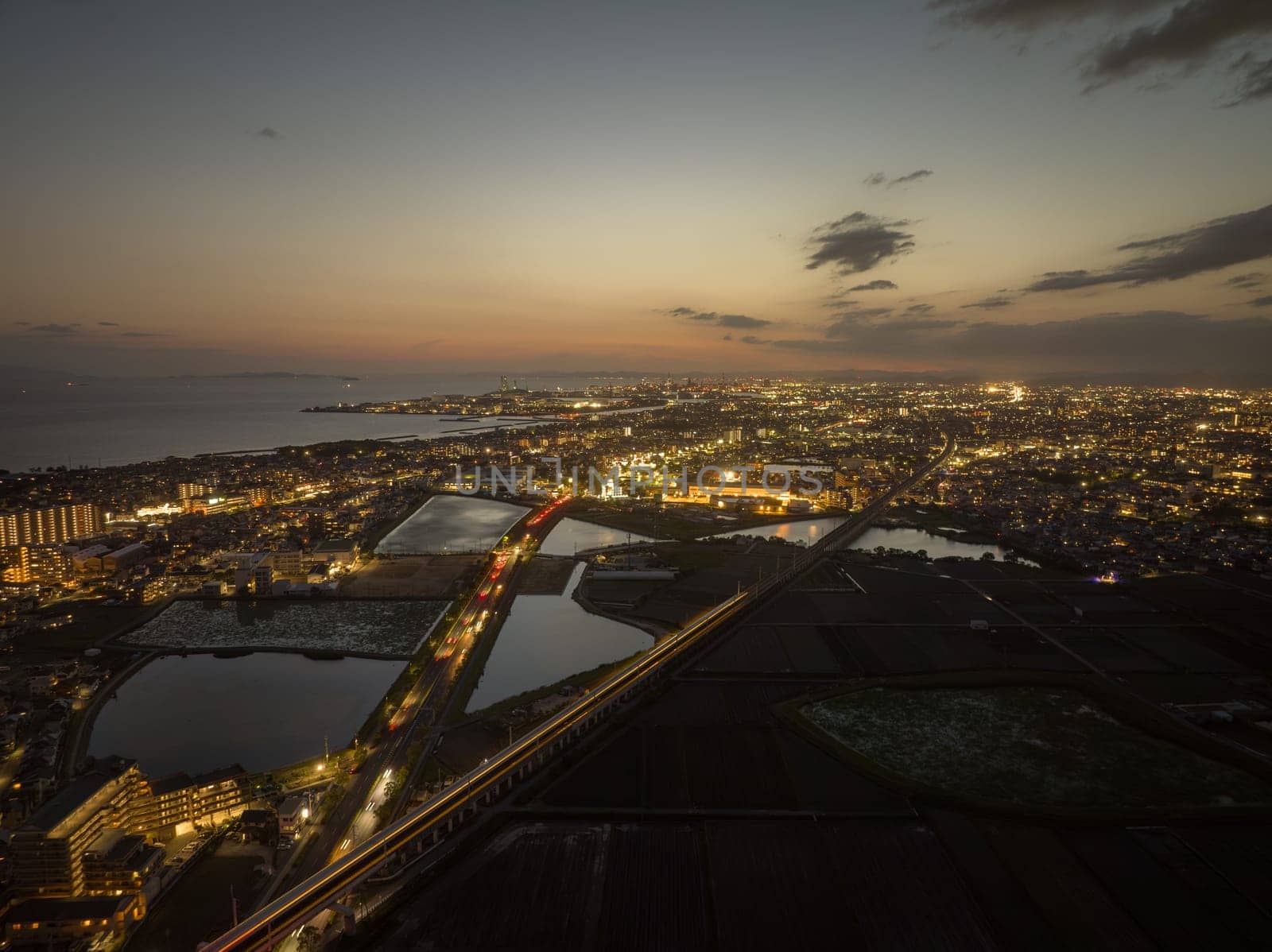 Lights from high speed train blur past vehicle traffic to city at sunset. High quality photo