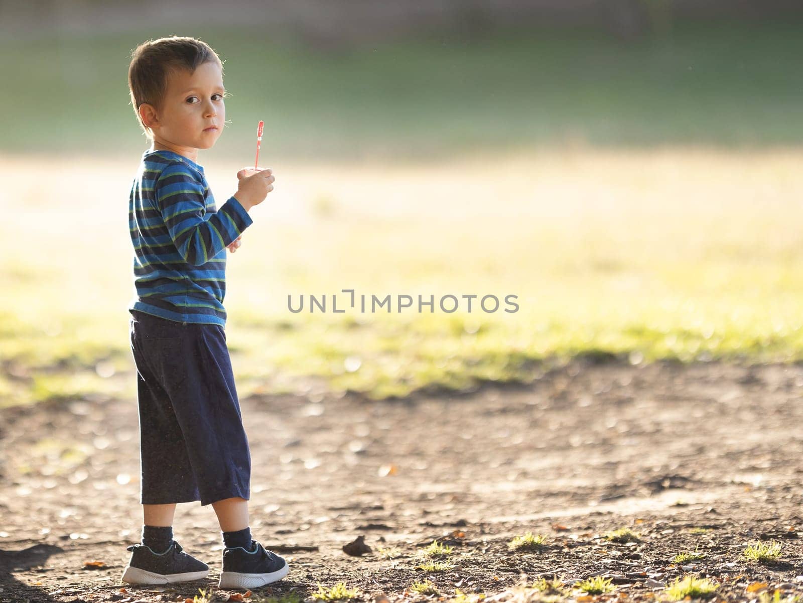 Little boy with a soap bubble stick standing in the park and looking in the camera. Mid shot