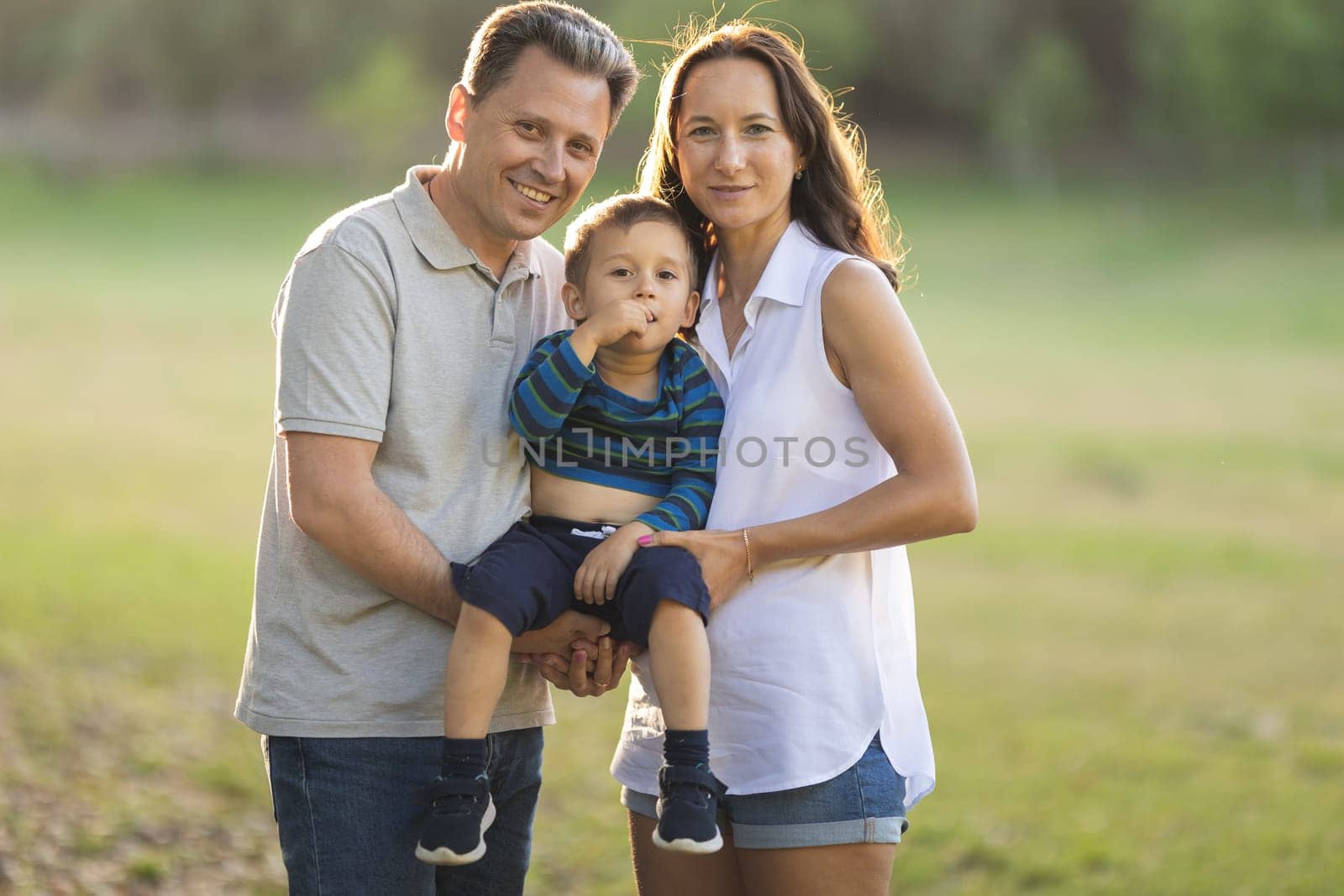Cute white parents holding their little son on their arms in the park by Studia72