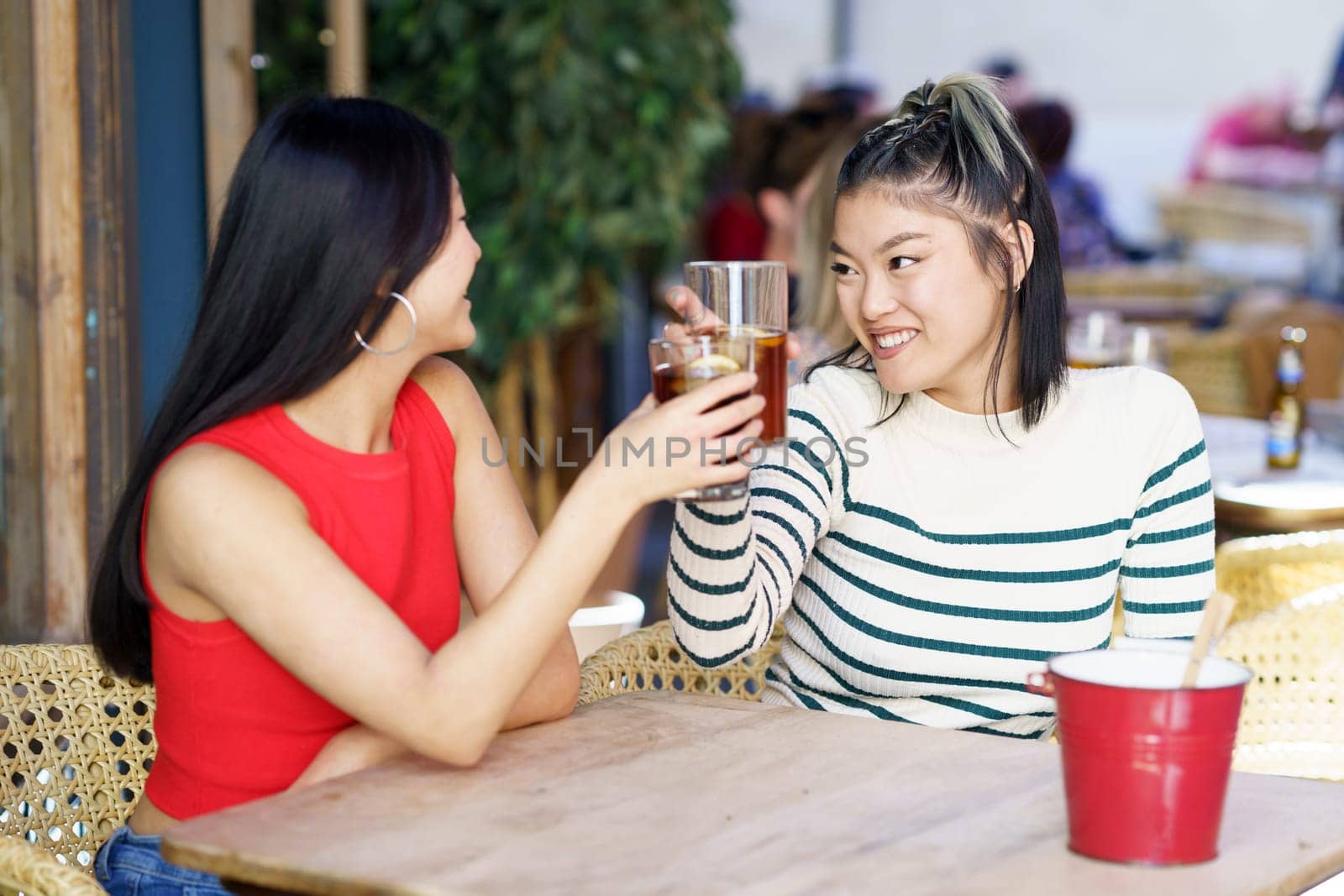 Joyful Asian women clinking glasses of cold tea in cafe by javiindy