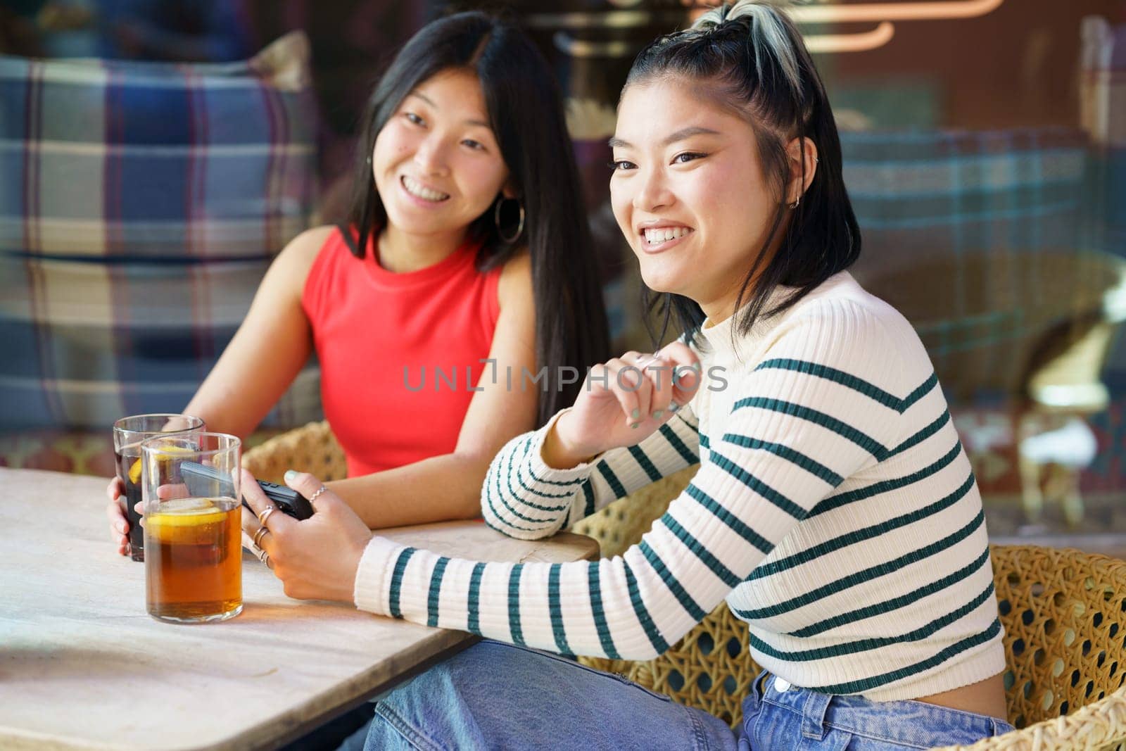 Two young Chinese women having a drink on the terrace of a typical bar in Granada. Concept of Asian people traveling in Europe.