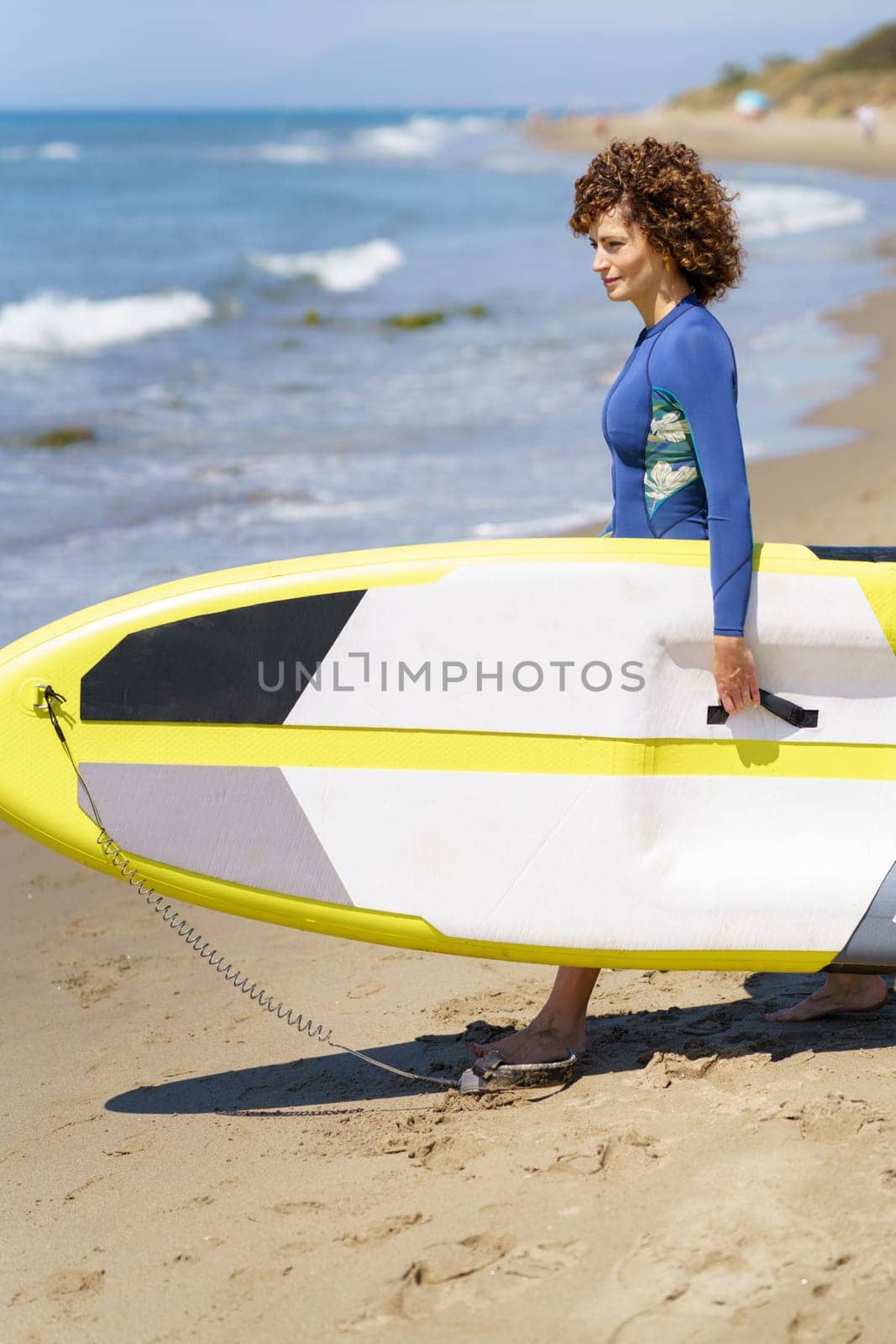 Female surfer holding paddleboard on sandy beach by javiindy
