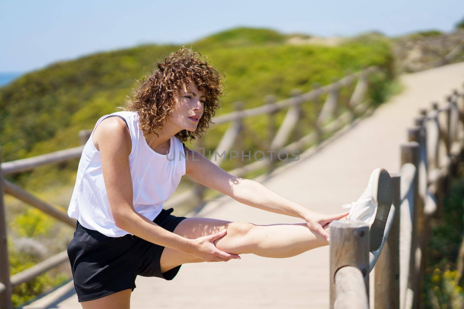 Focused young woman stretching leg on wooden bridge by javiindy