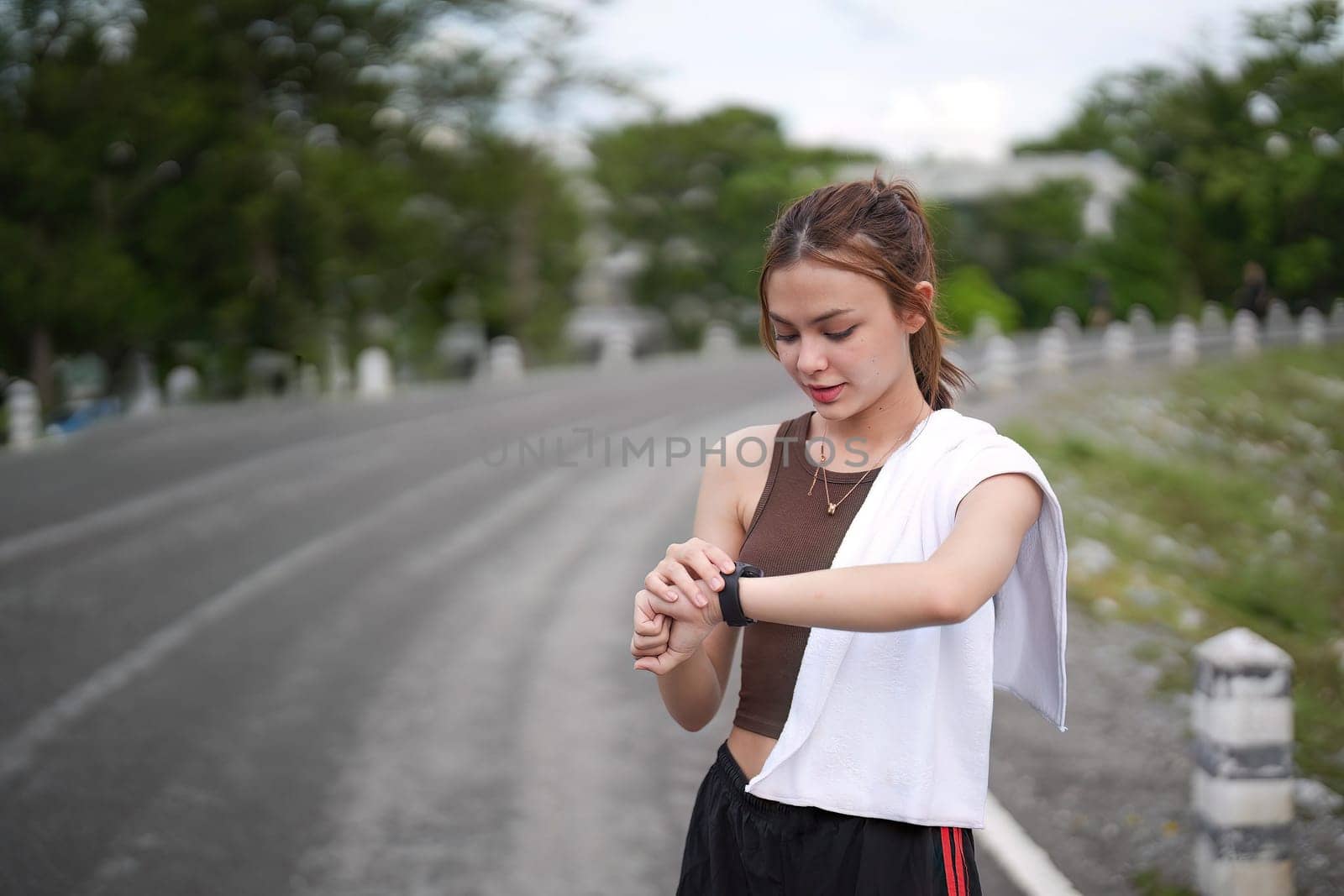 Young woman jogging and looking at her smart wrist watch, copy space, outdoor.