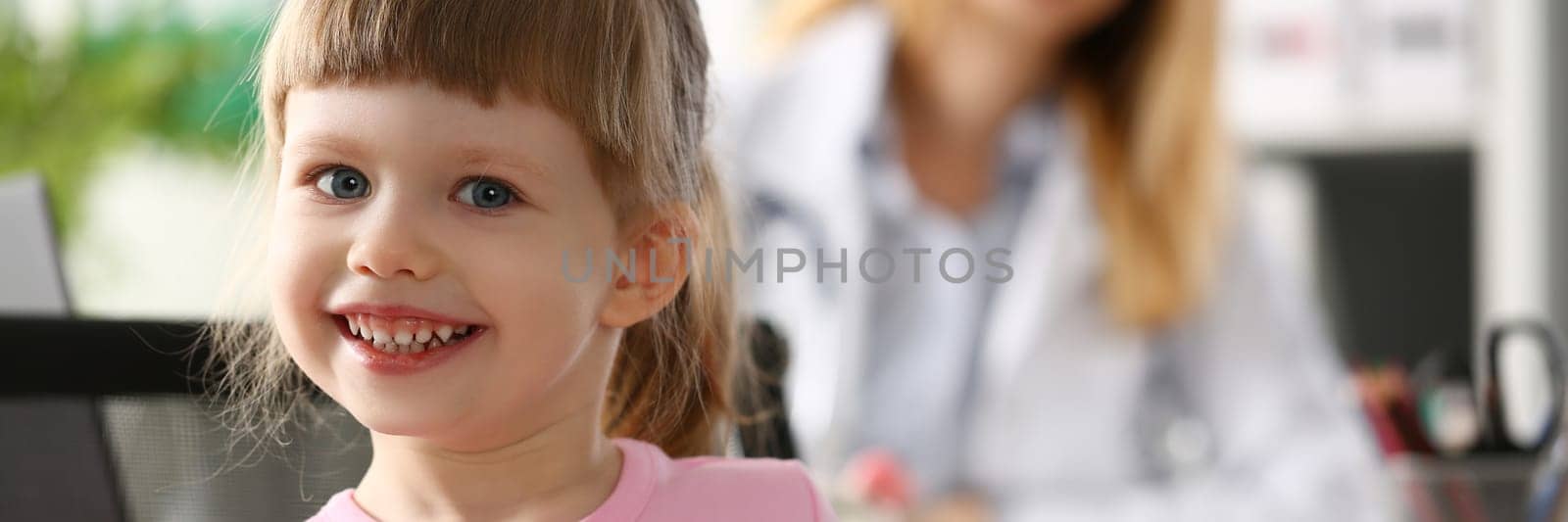 Portrait of little smiling baby girl in background sits doctor. Children health insurance and pediatrician services
