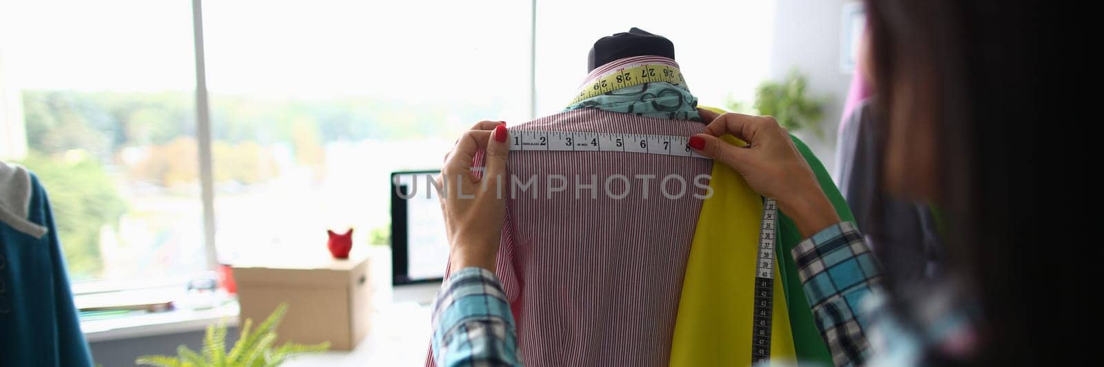 Woman fashion designer seamstress stylist measuring mannequin with tape. Working with mannequin in cozy creative design studio or atelier concept