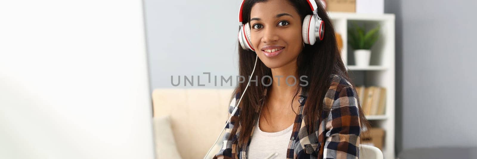 African female student wears headphones studying alone at home office desk. Mixed race woman listening to audio podcast and learning english language concept and taking notes concept