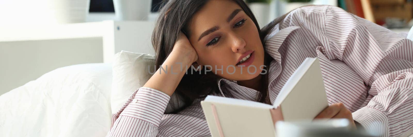 Beautiful woman lies in bed and reads book by kuprevich