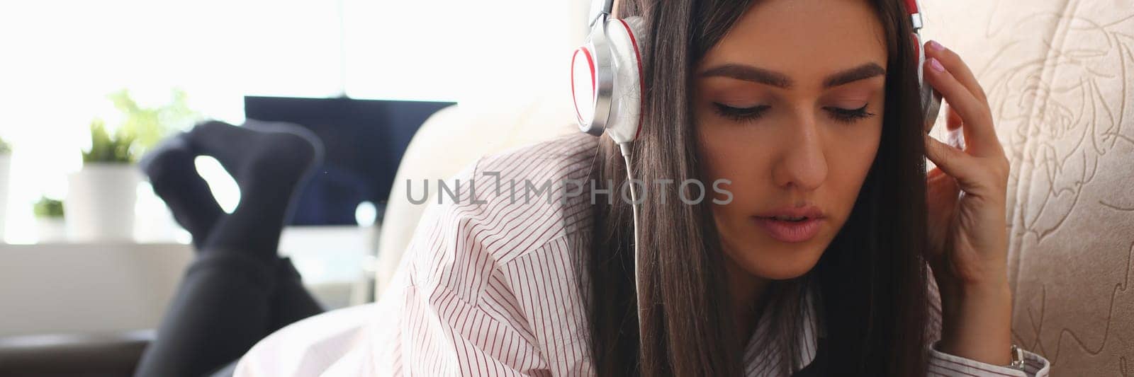 Young woman in headphones is relaxing on sofa and listening to music online using smartphone by kuprevich