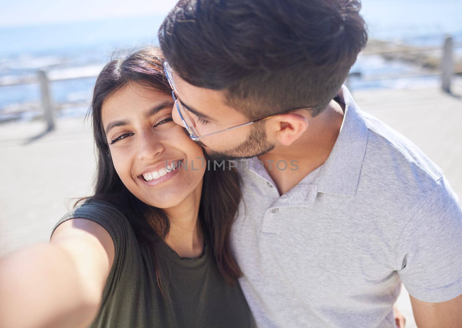 Couple, love and selfie at the beach, travel and kiss by ocean with support, trust and care with adventure in Mumbai. Smile in picture, happy and memory with smartphone photography for romance by YuriArcurs
